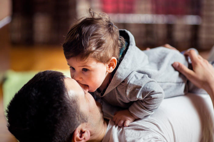 This stock image shows a baby and father playing at home. New research finds that babies judge the relationship between two people by whether or not they willingly share saliva.