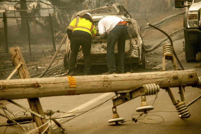 In this Nov. 10, 2018 file photo, with a downed power utility pole in the foreground, Eric England, right, searches through a friend's vehicle after the wildfire burned through Paradise, Calif.