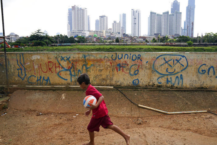 A young boy plays as high rise buildings at the main business district are seen in the background, in Jakarta, Indonesia, Tuesday, Jan. 25, 2022.