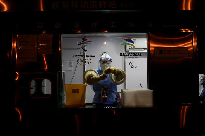 A worker prepares to administer a COVID-19 test at the 2022 Winter Olympics on Wednesday. So far, 111 athletes and officials have tested positive for the virus at the Olympics, including from people arriving at the airport.