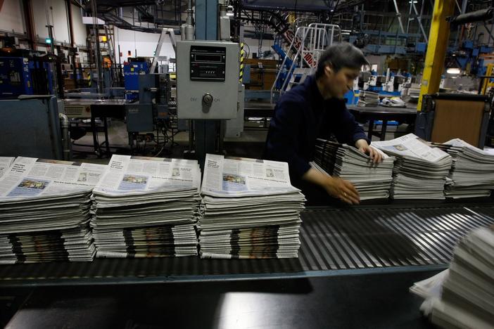 A worker at a <em>San Francisco Chronicle</em> printing plant arranges stacks of freshly printed newspapers in 2007. Its digital version, like that of so many newspapers', is behind a paywall.