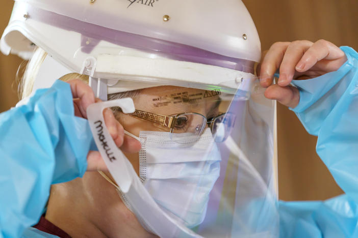 Nursing assistant Michelle Bryan dons a protective face shield before entering the room of a COVID-19 patient on the acute care floor.