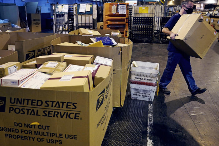 A worker carries a large parcel at the U.S. Postal Service sorting and processing facility in Boston on Nov. 18, 2021.