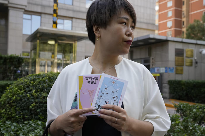 Teresa Xu holds up cards, one of which reads "My Womb, My Choice," before attending a court session at the Chaoyang People's Court in Beijing, Sept. 17, 2021. Xu is suing a public hospital for the right to freeze her eggs after it refused to do so because she isn't married.