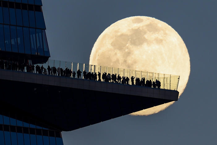 The moon rises on Tuesday behind people standing on The Edge, the outdoor observation deck in Manhattan.