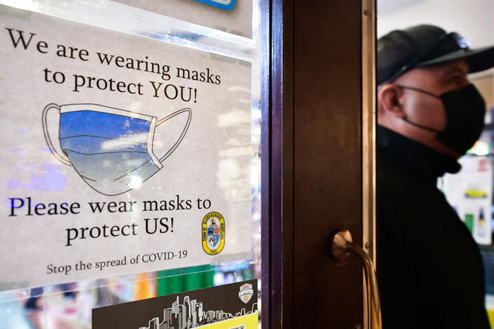 A man wears his mask as he walks past a sign posted on a storefront reminding people to wear masks, on February 25, 2022 in Los Angeles. Los Angeles ends its indoor mask mandate on February 25 for fully vaccinated people with proof of vaccination. Masks are still required for unvaccinated people or those who cannot show proof of a negative test.