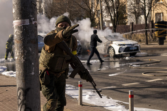 Ukrainian soldiers take positions outside a military facility as two cars burn in a street in Kyiv, Ukraine, on Saturday.