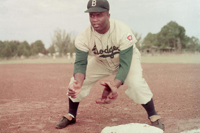 American professional baseball player Jackie Robinson of the Brooklyn Dodgers, dressed in a road uniform, crouches by the base and prepares to catch a ball in 1951.
