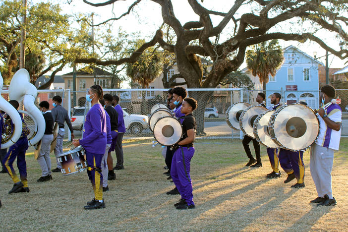 Warren Easton Charter High School's marching band members line up in formation. Their instruments, among many, include sousaphones, cymbals, and a drum section with snare, tenor and bass drums.