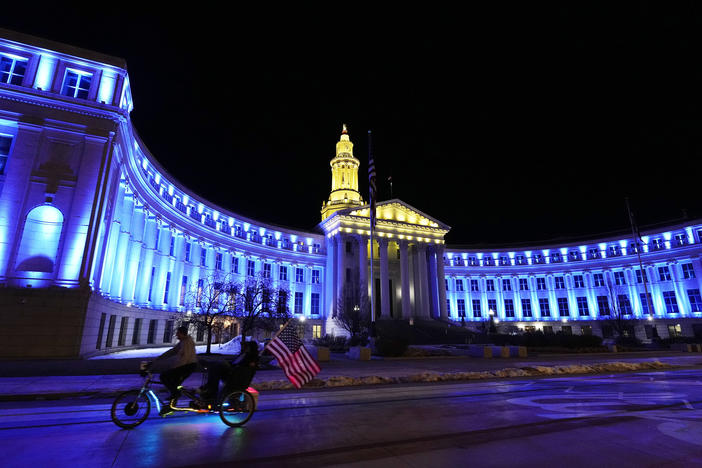 An American flag unfurls off a pedicab as it glides past the Denver City/County Building, which is illuminated in yellow and blue in support of Ukraine on Monday. Colorado's State Capitol will also be illuminated in blue and yellow in support of Ukraine.