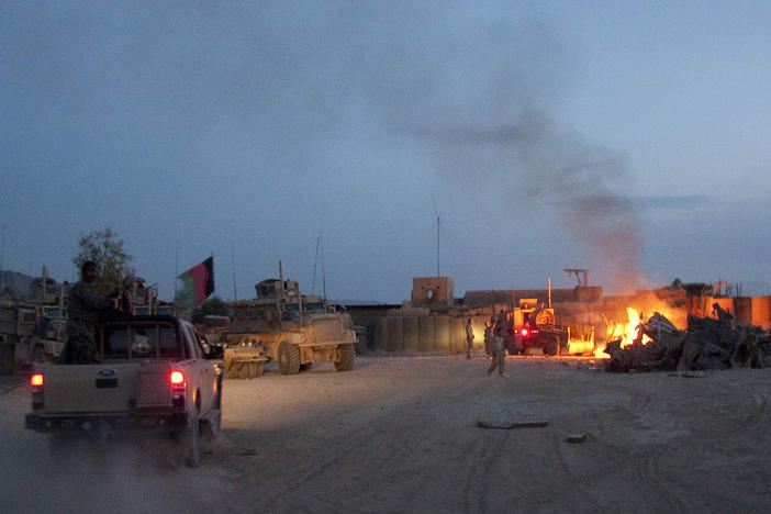 In this April 28, 2011, photo, an Afghan national army pickup truck passes parked U.S. armored military vehicles as smoke rises from a fire in a trash burn pit at Forward Operating Base Caferetta Nawzad, Helmand province south of Kabul, Afghanistan.