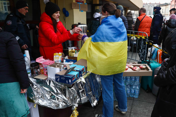 A woman wearing the Ukrainian flag is handed a beverage at the train station in Przemysl, Poland,  on Thursday. Ukrainians have been welcomed into Poland and other neighboring countries as they flee Russian attacks.