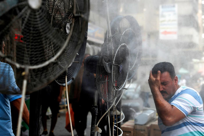 Fans spray air mixed with water vapor to cool down pedestrians on a Baghdad street on June 30, 2021, during a heat wave.