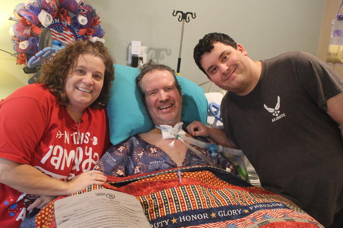 Lara and Trey Garey stand at the bedside of Tom Garey, an Air Force veteran with advanced ALS. Trey, 19, has spent much of his teenage years caring for his father at their Texas home.