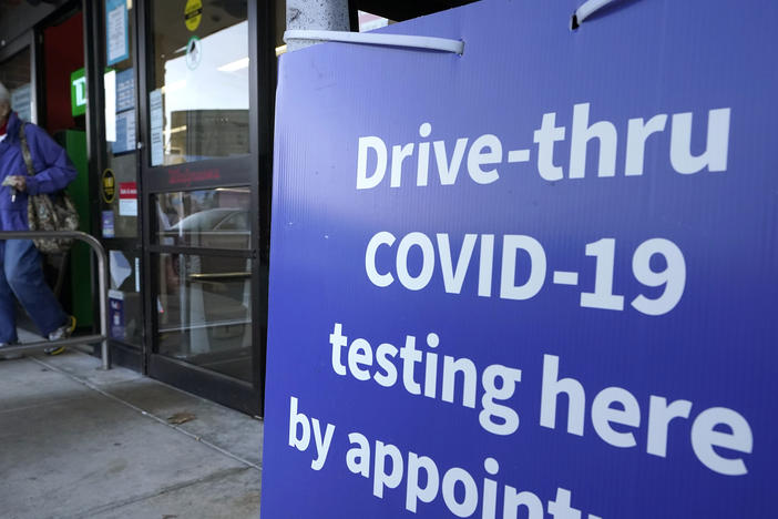 A passer-by walks past a sign that calls attention to COVID-19 testing while departing a Walgreens pharmacy, Wednesday, Dec. 15, 2021, in New Bedford, Mass. (AP Photo/Steven Senne)