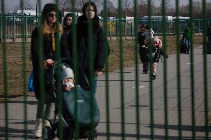 Refugees walk toward a green steel fence that marks the end of a buffer zone between Ukraine and Medyka, Poland.