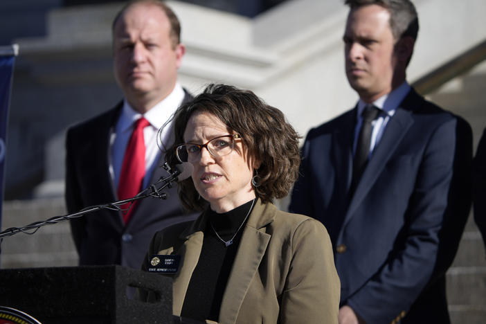 Colorado Governor Jared Polis, back left, and Colorado Senate Majority Leader Steve Fenberg, back right, listen as Majority Leader Daneya Esgar speaks during a news conference. Esgar has called for the U.S. Supreme Court to uphold <em>Roe v. Wade</em>.