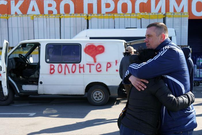 Olga and Oleksandr hug as they wait beside a vehicle painted with the word "volunteers" at an evacuation center in Zaporizhzhya, Ukraine, on Tuesday. Olga's father is stuck in Mariupol, and Oleksandr is hoping to get in a volunteer convoy to the city, now under Russian siege.