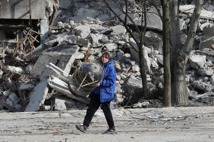 A local resident carries a cage on Thursday while walking past an apartment building destroyed in the besieged city of Mariupol.