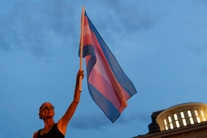 Cole Ramsey, 39, of South Linden, Ohio, holds a Transgender Pride Flag in front of the Ohio Statehouse in Columbus to protest the passing of legislation against trans women playing sports in high school and college.