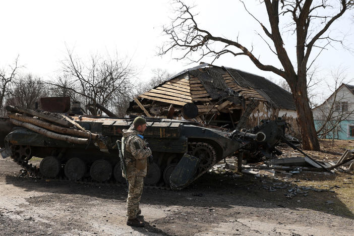 A Ukrainian soldier stands in front of a destroyed Russian armored personnel carrier in a village on the frontline of the northern part of the Kyiv region on Monday. Russia says its troops are starting to withdraw from Kyiv, thought the Pentagon believes they will likely be deployed elsewhere in Ukraine.