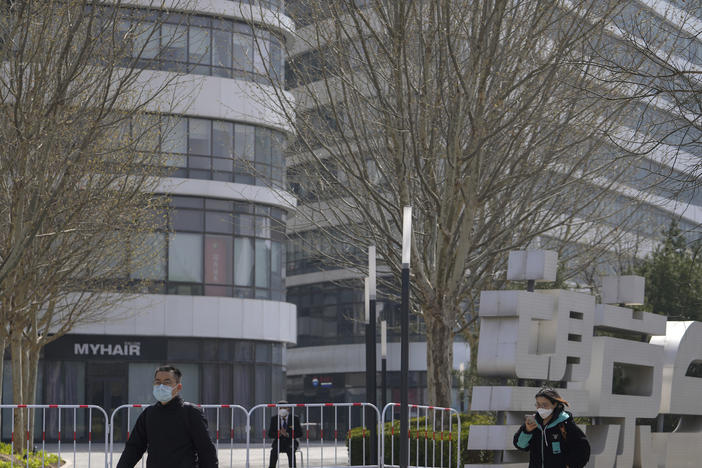 Residents wearing face masks walk by a masked security watch over a barricaded Galaxy Soho commercial office building locked down for health monitoring following a COVID-19 case detected in the area Tuesday in Beijing. China has sent more than 10,000 health workers from across the country to Shanghai, including 2,000 military medical staff.