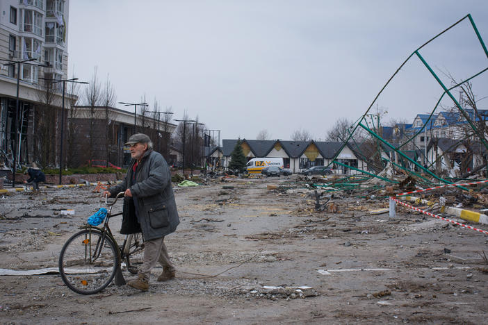 A man walks his bike through a parking lot littered with broken glass in Bucha, Ukraine.