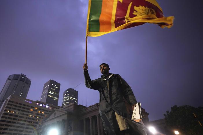 A man waves a Sri Lankan national flag as he stands on a barricade blocking the entrance to president's office during a protest in Colombo, Sri Lanka on Monday.