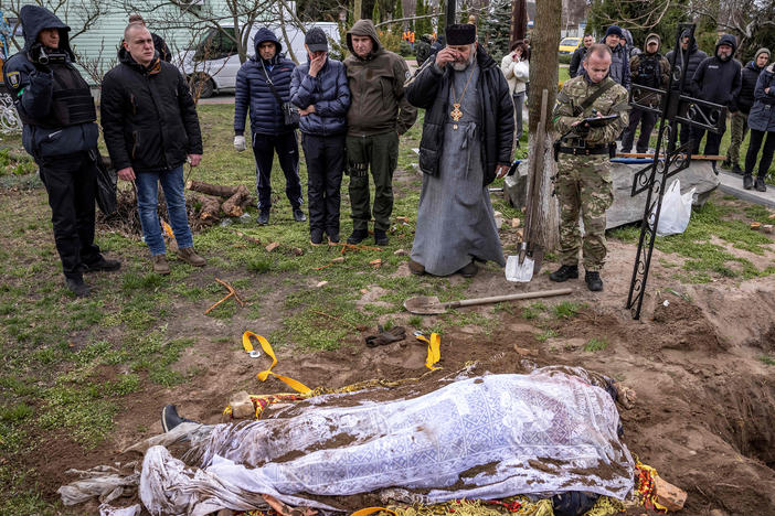 A priest and relatives on Tuesday stand near the exhumed body of Gostomel's mayor, Yuriy Prylypko, who had been buried near a church in the village in the Kyiv region. Prylypko, 62, was killed on March 7 after Russian forces rolled into his village.