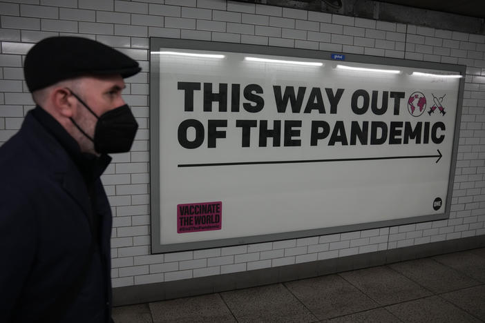 A man wearing a face mask to curb the spread of coronavirus walks past a health campaign poster in the Westminster underground train station, in London.