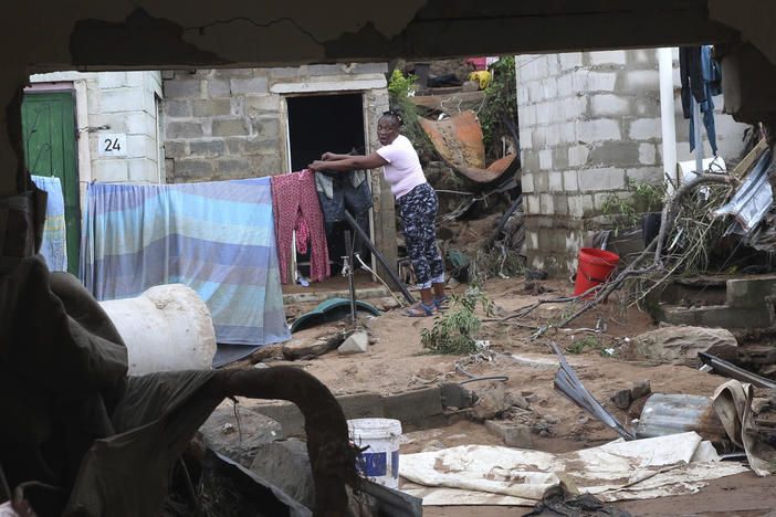 A woman is seen through a damaged wall hanging her clothes on a makeshift washing line in Ntuzuma, outside of Durban, South Africa, on Wednesday. Flooding in South Africa's Durban area has taken killed at least 259.