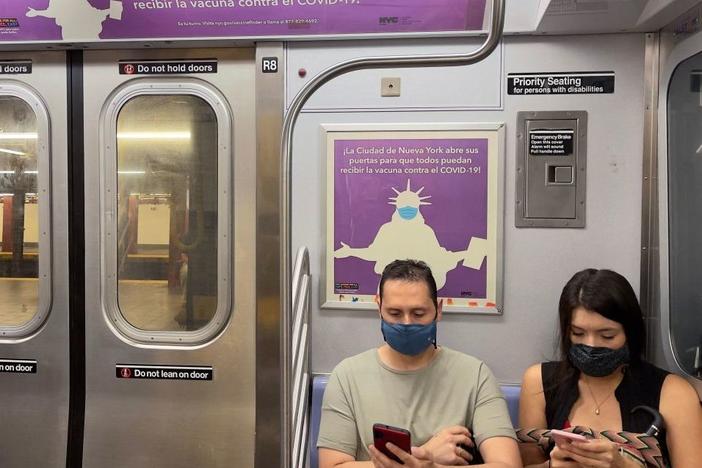 Travelers wearing masks sit in the subway where posters advertise free COVID-19 vaccination in New York City in several languages on July 18, 2021.