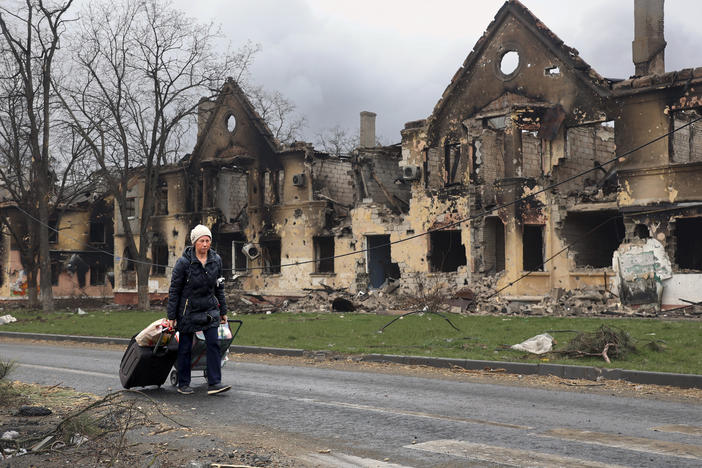 A woman on April 8 pulls her baggage past houses damaged during fighting in Mariupol, Ukraine.