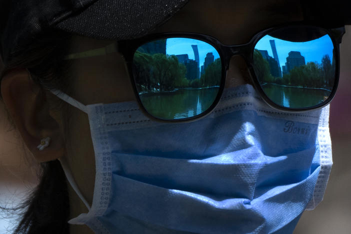 The skyline of Beijing is reflecting in the sunglasses of a woman wearing a face mask as she walks at a public park in Beijing, Thursday, April 14, 2022.