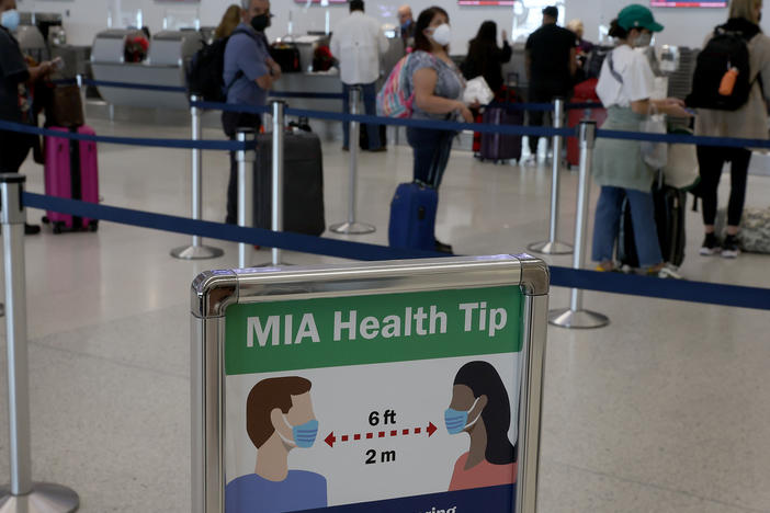 A sign advises people to wear a mask and stand six feet apart as travelers make their way through Miami International Airport in December 2021 in Miami. A federal judge in Florida has ruled that the federal mask mandate on planes, trains, buses and other modes of public transportation is unlawful.