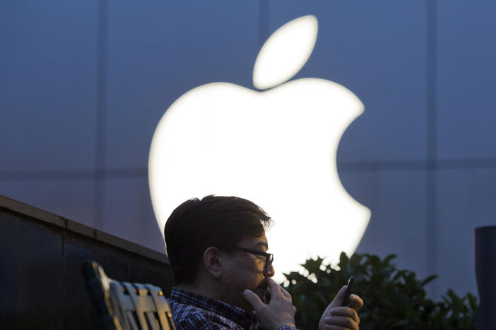 A man uses his mobile phone near an Apple store logo in Beijing.