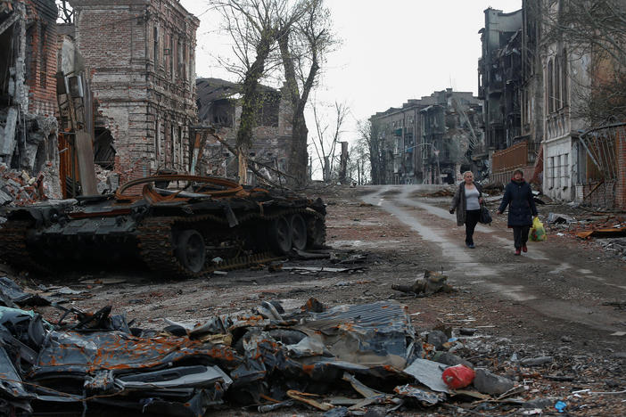 People walk near a destroyed tank and damaged buildings in the southern port city of Mariupol, Ukraine, on Friday.