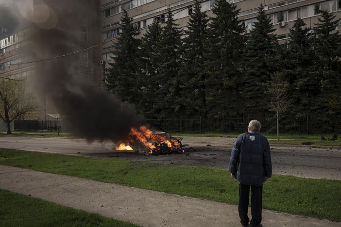A man watches as a car burns with two people inside, after a Russian bombardment in Kharkiv, Ukraine, Thursday, April 21, 2022.