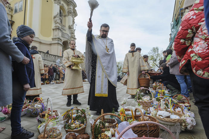 A Ukrainian priest blesses believers as they collect traditional cakes and painted eggs prepared for an Easter celebration in the in Lviv, Ukraine, Saturday, April 23, 2022.