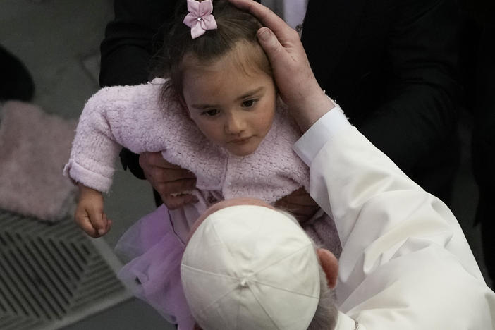 Pope Francis caresses a child in the Paul VI hall at the Vatican, Friday, April 8, 2022. Italy's Constitutional Court ruled that children should receive both parents' surnames at birth, not just the father's.