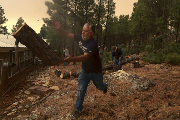 Chris Castillo throws a freshly cut log as he and his cousins clear a wireline along a family member's home in Las Vegas, N.M., on Monday. Wind-whipped flames are marching across more of New Mexico's tinder-dry mountainsides, forcing the evacuation of area residents.