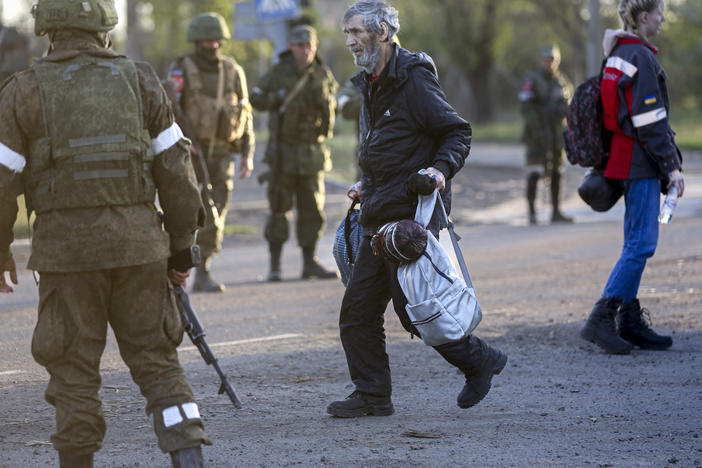 A man who left a shelter in the Azovstal steel plant in Mariupol walks to a bus between Russian army servicemen and Donetsk People's Republic militia on Friday.