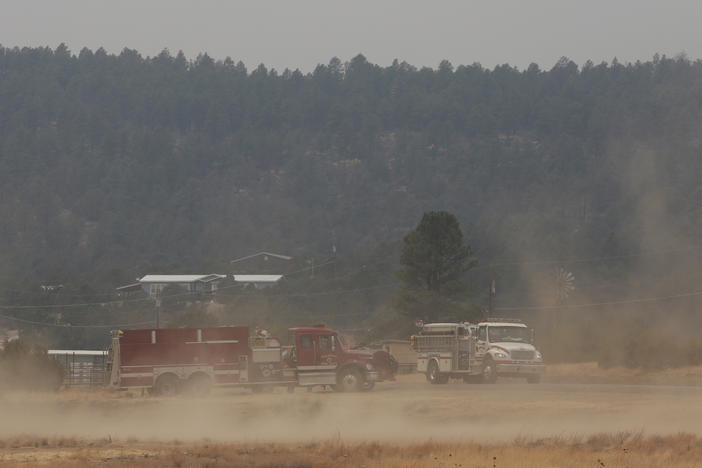 Wind kicks up dust at the fairgrounds as firefighters meet and confer about the wildfire raging on the other side of the hill behind them just outside of Las Vegas, N.M., on Saturday, May 7, 2022.