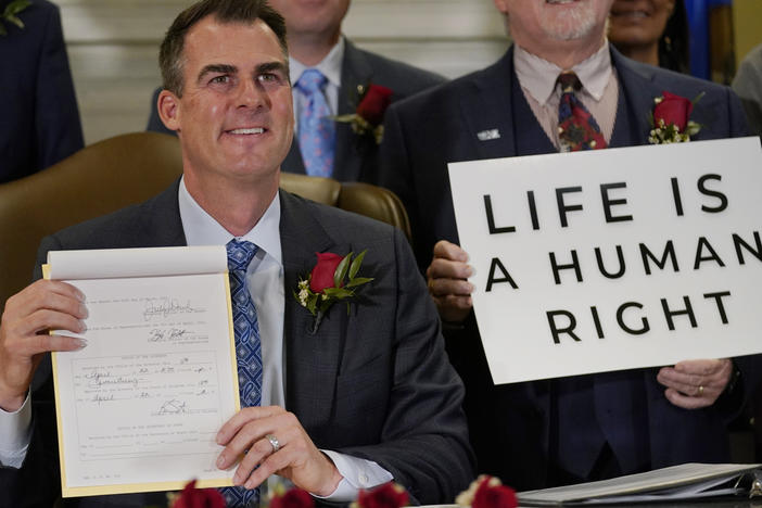 Oklahoma Gov. Kevin Stitt poses for a photo with the bill he signed, making it a felony to perform an abortion, punishable by up to 10 years in prison, on April 12, 2022, in Oklahoma City, following a bill signing ceremony.