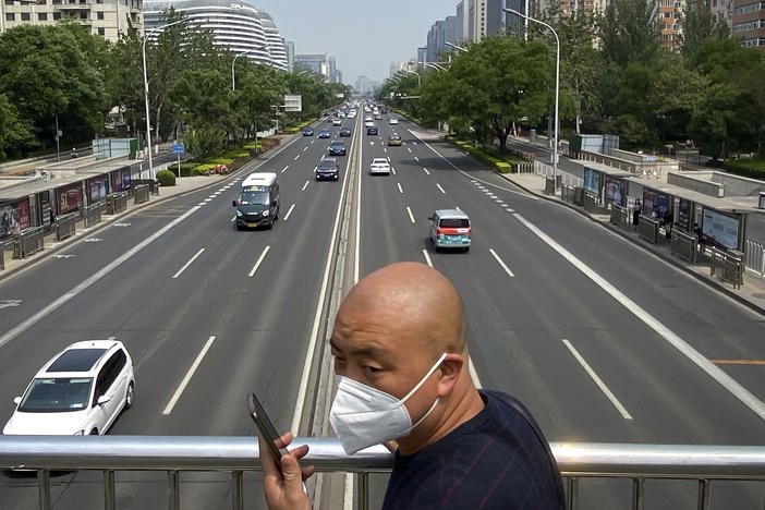 A man wearing a face mask stands on a bridge over an expressway in Beijing, Thursday, May 19, 2022. Parts of Beijing on Thursday halted daily mass testing that had been conducted over the past several weeks, but many testing sites remained busy due to requirements for a negative COVID test in the last 48 hours to enter some buildings in China's capital.