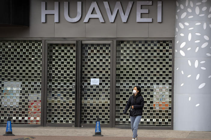 A woman wearing a face mask walks past a Huawei store temporarily closed due to coronavirus-related restrictions in Beijing, Thursday, May 12, 2022. China's leaders are struggling to reverse a deepening economic slump while keeping a "zero-COVID" strategy that has shut down Shanghai and other cities.