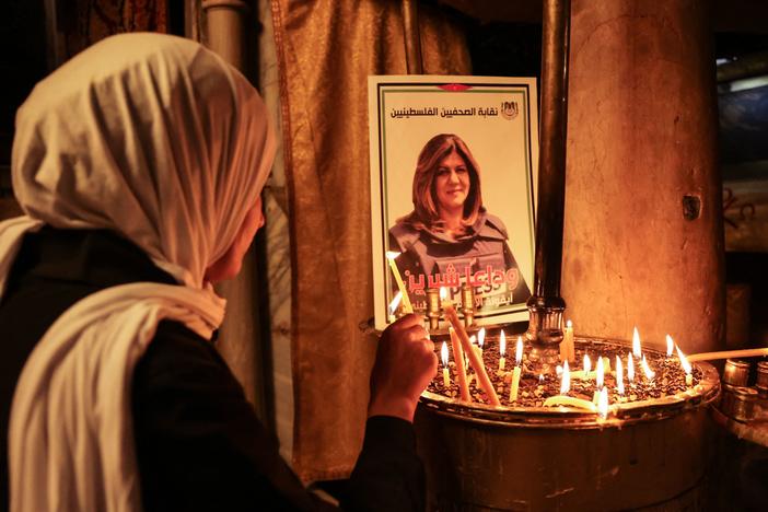 A woman lights a candle in front of a poster depicting Shireen Abu Akleh.