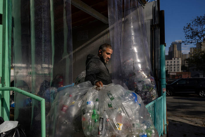A worker carries used drink bottles and cans for recycling at a collection point in Brooklyn, New York. Three decades of recycling have so far failed to reduce what we throw away, especially plastics.