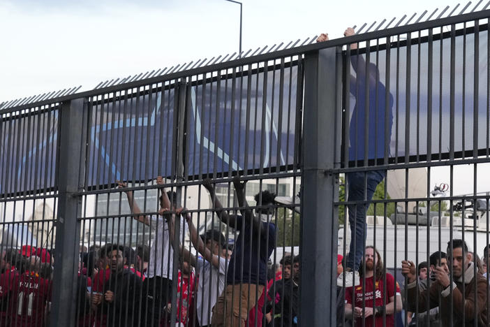 Fans climb on the fence in front of the Stade de France prior to the Champions League final soccer match between Liverpool and Real Madrid, in Saint Denis near Paris, Saturday, May 28, 2022.