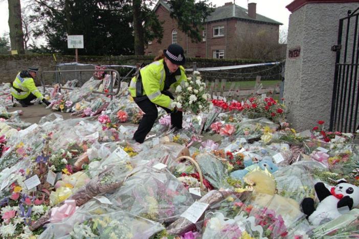A police officer arranges bouquets of flowers in rows at a side entrance to Dunblane Primary School following a school shooting that left 16 students and one teacher dead.